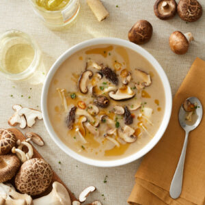 Lifestyle food photography of a hearty mushroom soup in a bowl, surrounded by fresh mushrooms, a glass of wine, and a napkin.