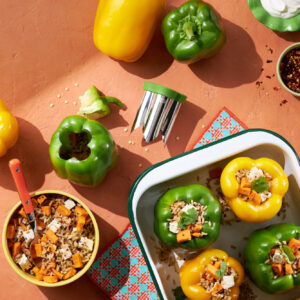 Stuffed green and yellow bell peppers in a studio food photography setup with ingredients and utensils on a terracotta surface.